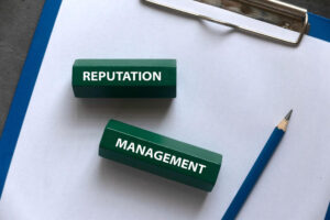 Words “reputation management” written on pieces of wood with a pencil and a clipboard in the background.