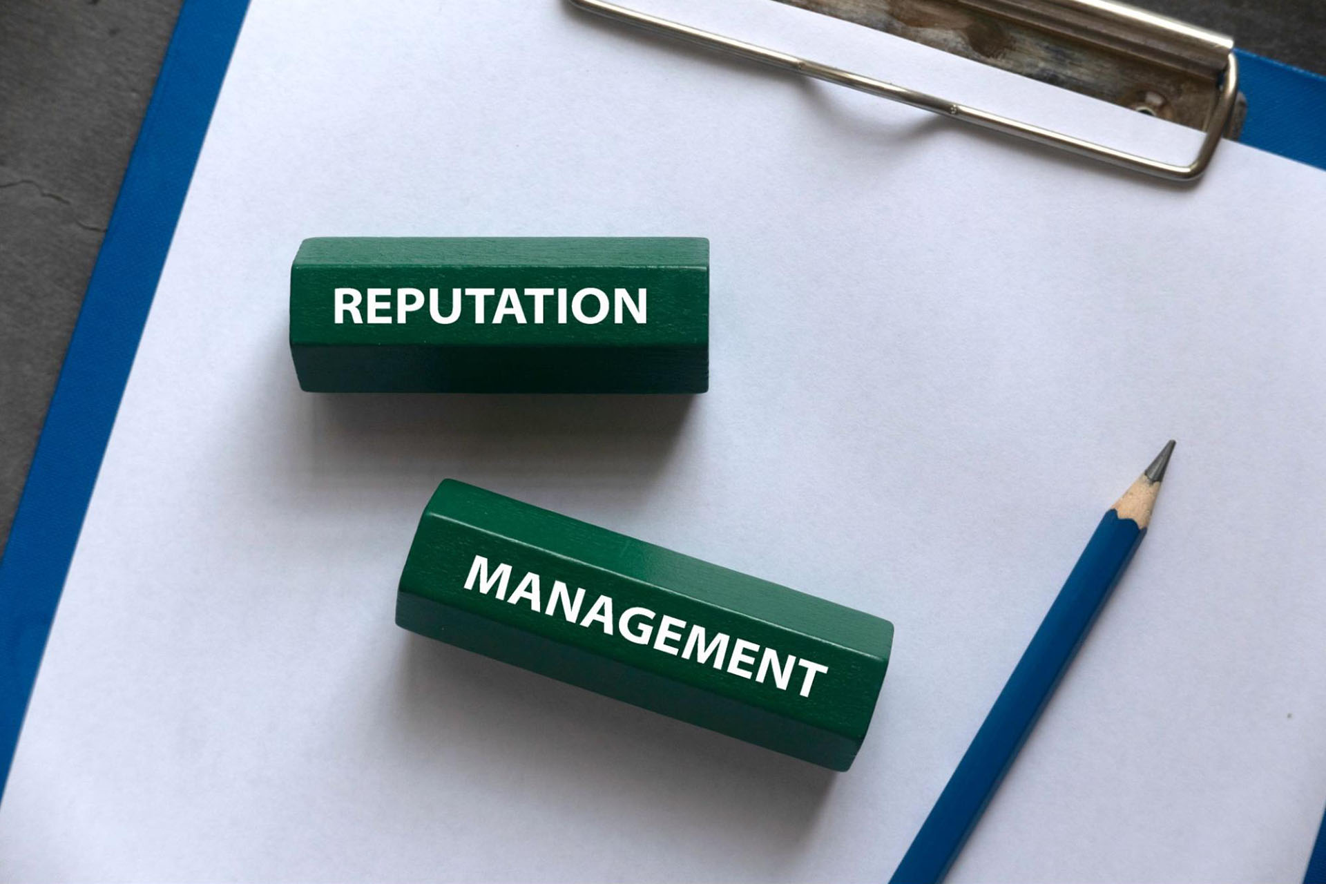 Words “reputation management” written on pieces of wood with a pencil and a clipboard in the background.